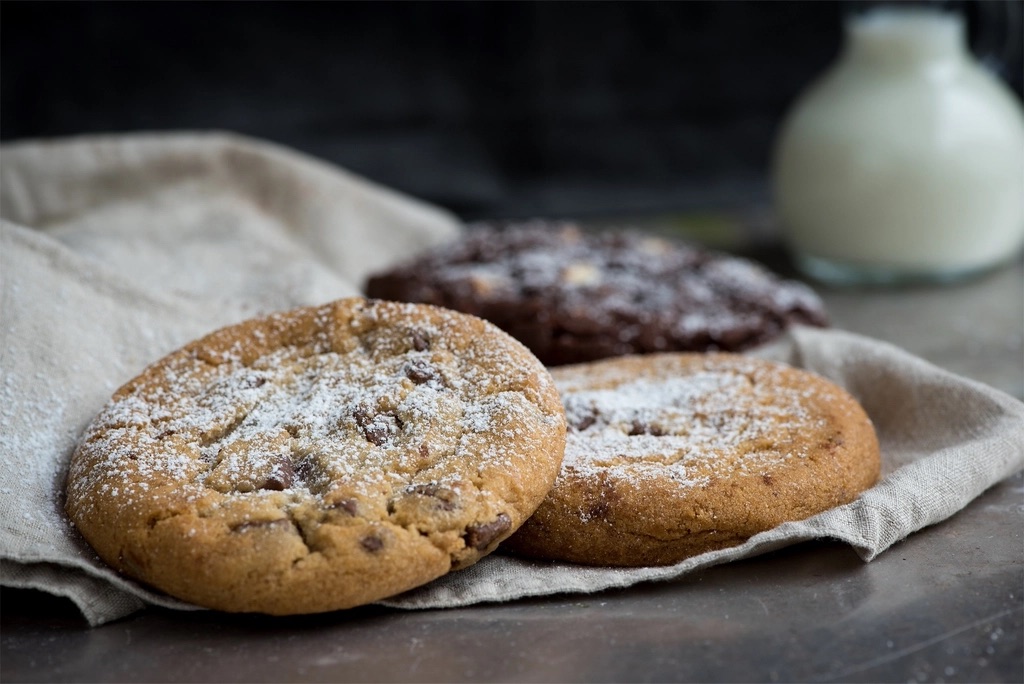 Brown butter chocolate chip cookies dusted with sugar on a linen napkin, with a jug of milk behind